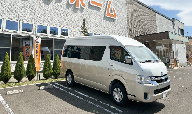 本社には、乗車定員10名のトヨタ・ハイエース グランドキャビンをベースにした社用車「あいホーム号（仮称）」を配備しています。研修や出張などの社内利用はもちろん、福利厚生として社員の私用利用も可能です。お子さまのスポーツ送迎など、家族のサポートにも活用されています。